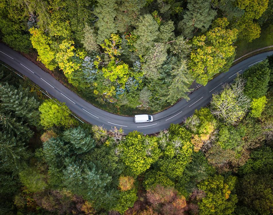 Aerial view of a car navigating a winding road surrounded by greenery and hills.