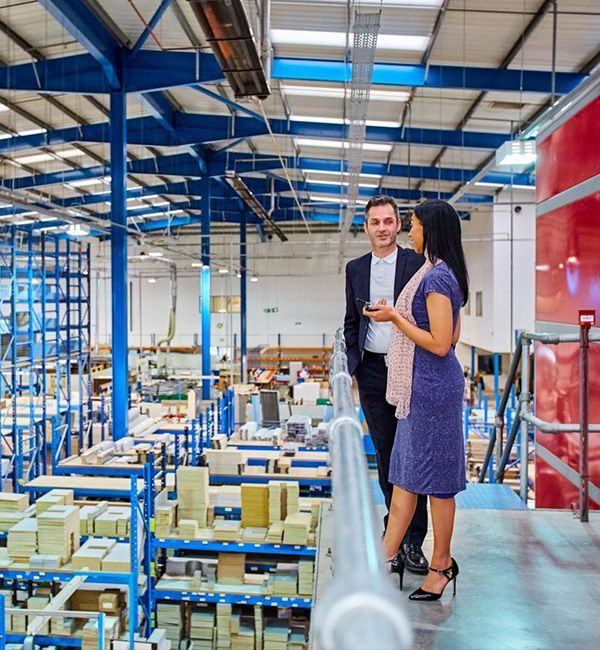 Two people are in a warehouse filled with boxes, engaged in conversation about the items stored there.