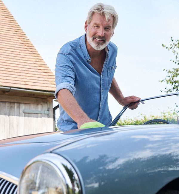 A man washes a classic car, focusing on its shiny exterior and vintage design.